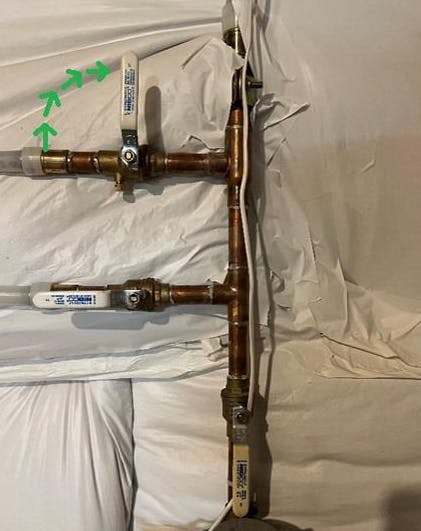 Copper pipes with valve handles and arrows indicating flow direction, wrapped in white material.