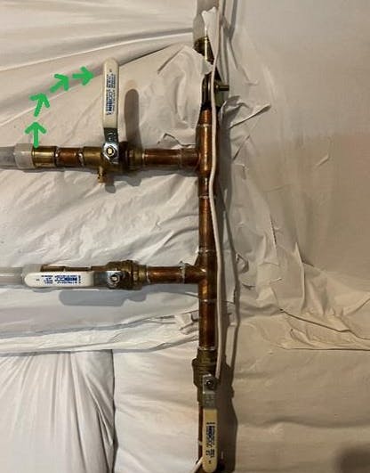 Copper pipes with valve handles and arrows indicating flow direction, wrapped in white material.
