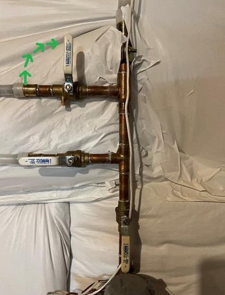 Copper pipes with valve handles and arrows indicating flow direction, wrapped in white material.