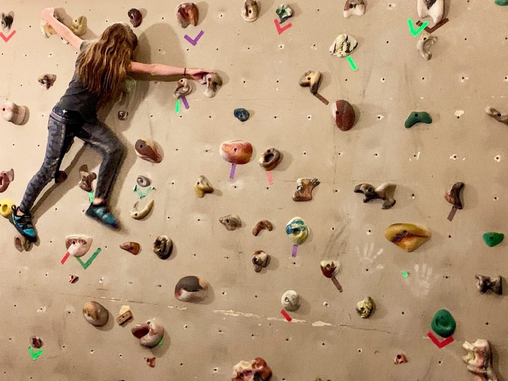 A person is bouldering on an indoor climbing wall with colored holds.