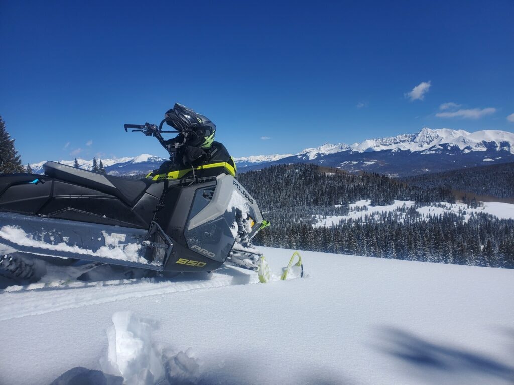 Snowmobile on a snowy mountain landscape with clear blue sky and distant mountains.