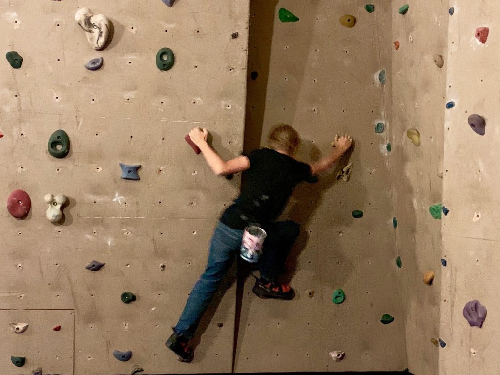 Person climbing an indoor rock wall with colorful holds.