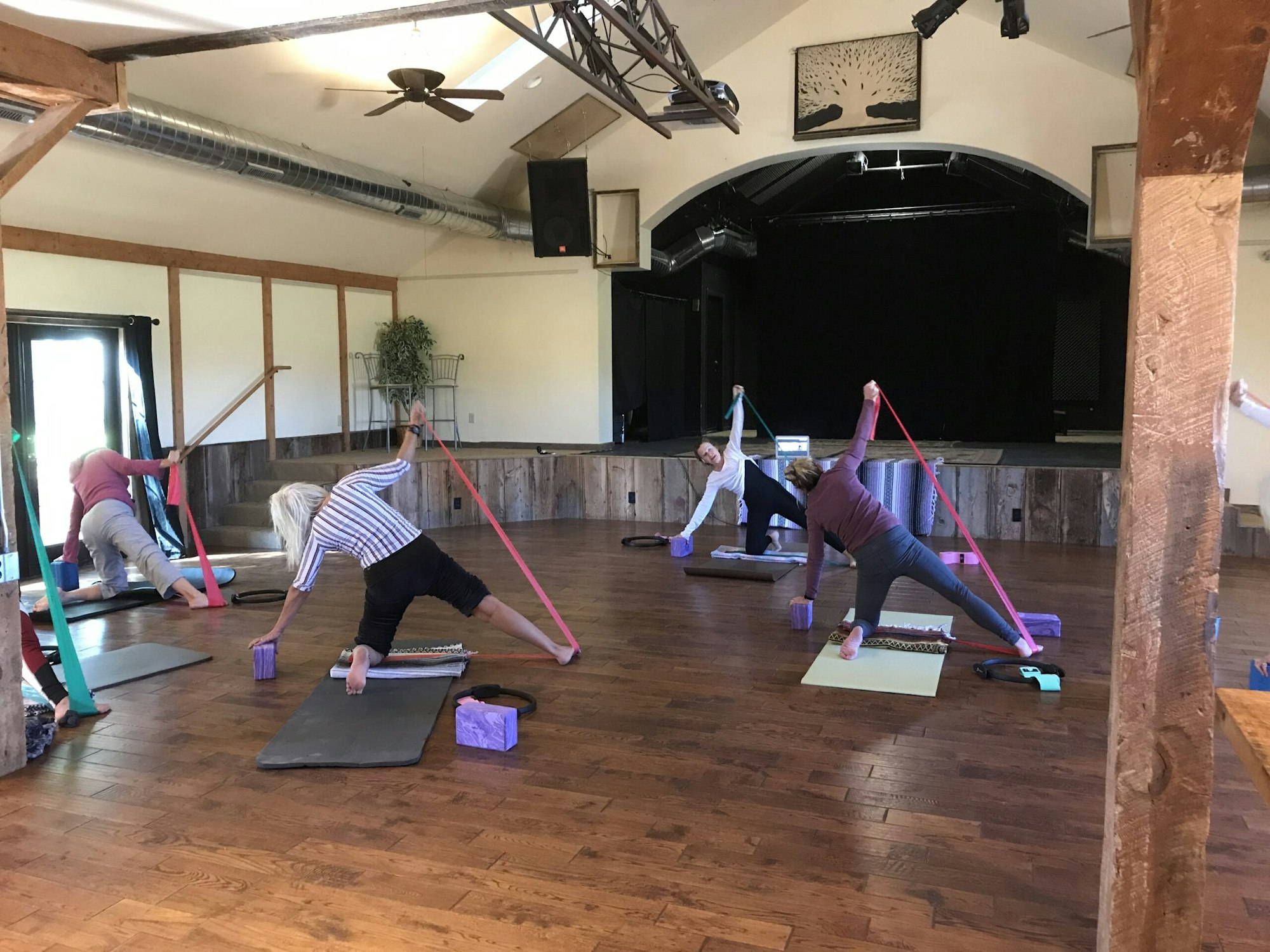 People practicing yoga with resistance bands in a spacious wooden studio.