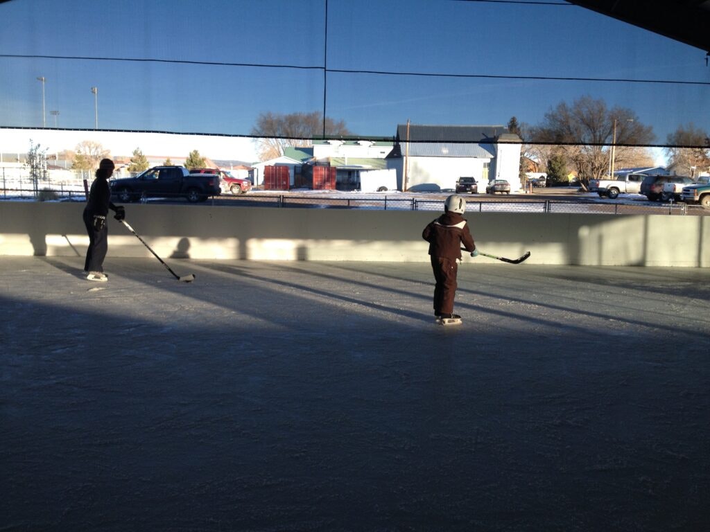 Two people playing hockey on an outdoor rink during the day.