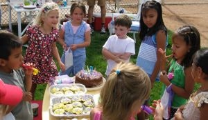 Children at a birthday party gathered around a table with cake and treats.
