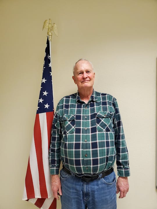 A person in a plaid shirt standing near an American flag.