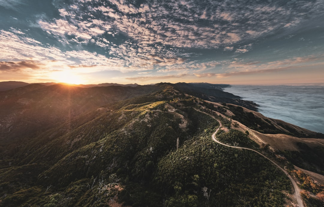 A breathtaking landscape featuring rolling hills, winding paths, and a stunning sunset over a valley clouds.