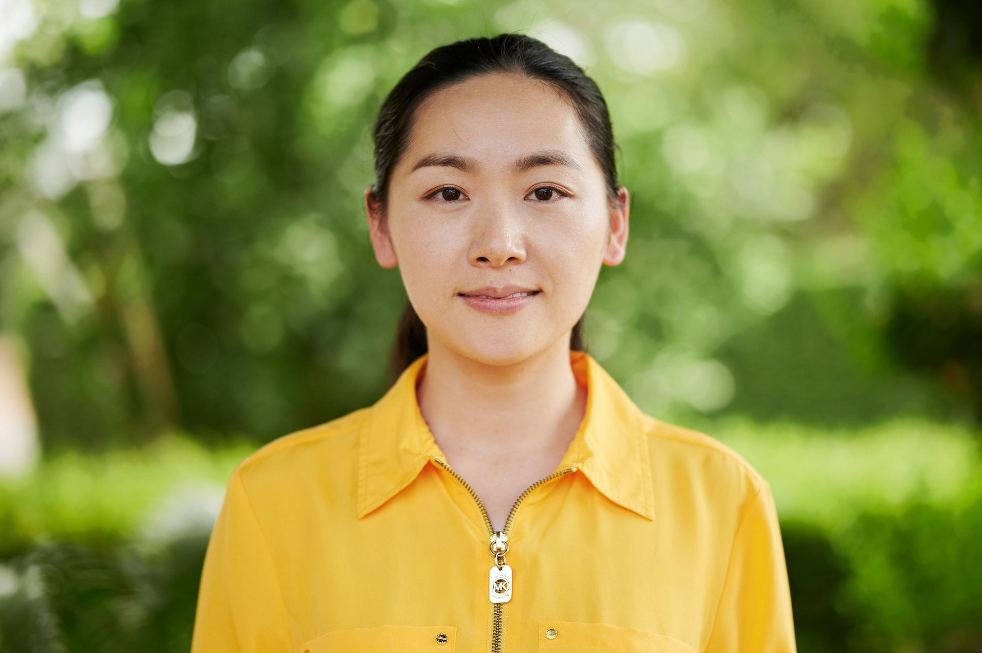 The image features a woman wearing a yellow shirt with a zipper, set against a green blurred background.