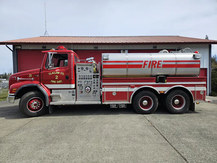 A red fire truck with a water tank and various controls parked outside a fire station.