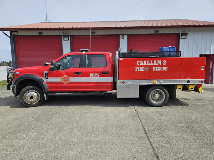 The image shows a red fire rescue truck with "Clallam 2 Fire Rescue" written on the side, parked in front of a fire station.