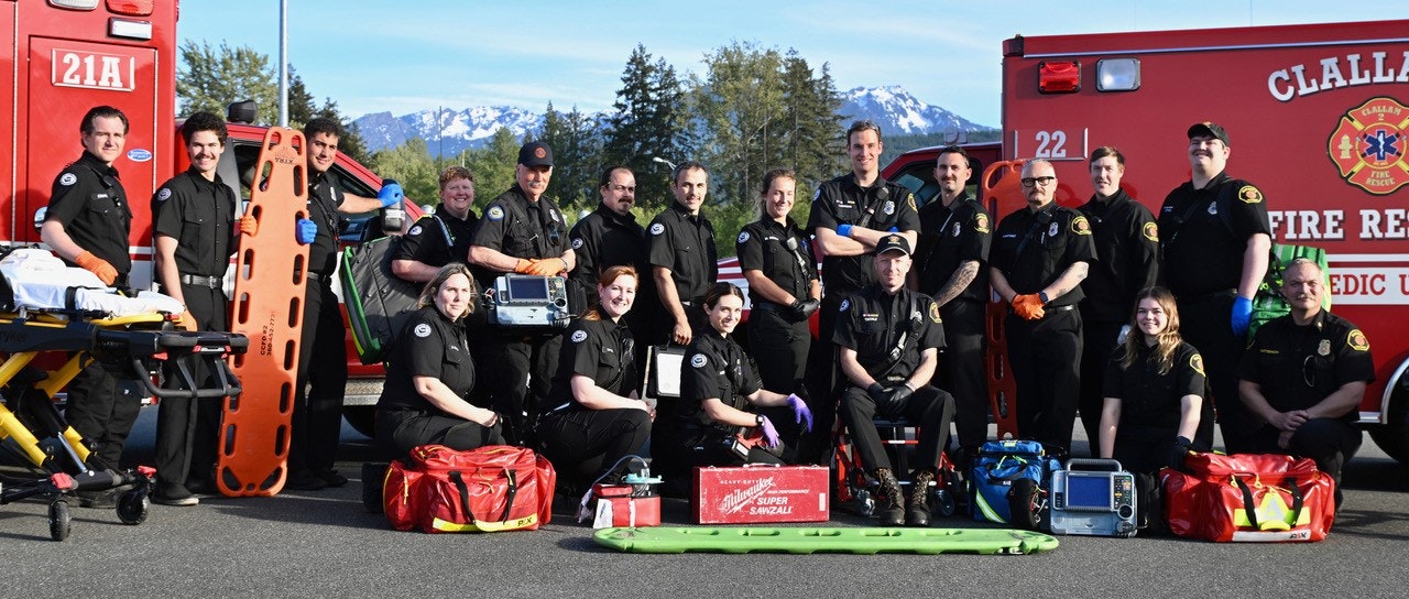A group of paramedics with emergency equipment and an ambulance, with mountains in the background.