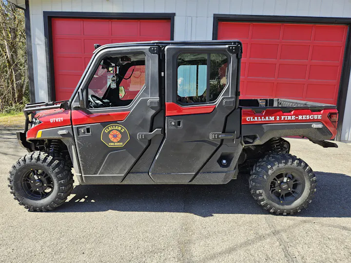 An ATV labeled "CLALLAM 2 FIRE-RESCUE" parked in front of a building with red garage doors.