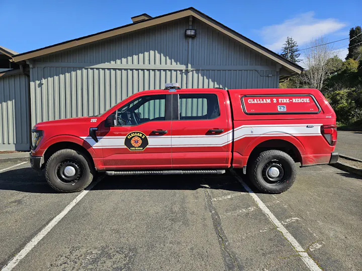 A red fire-rescue truck parked outside a building, identified as "Clallam 2 Fire-Rescue." Clear skies in the background.