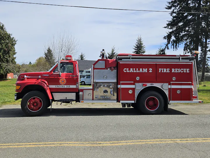 A red fire truck labeled "Clallam 2 Fire Rescue" parked on a street, featuring emergency lights and firefighting equipment.