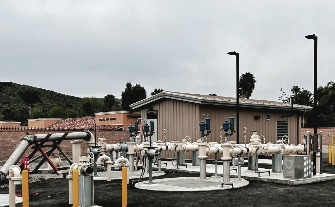 Lift station site with pipes, valves, and a building; water treatment or pumping facility.