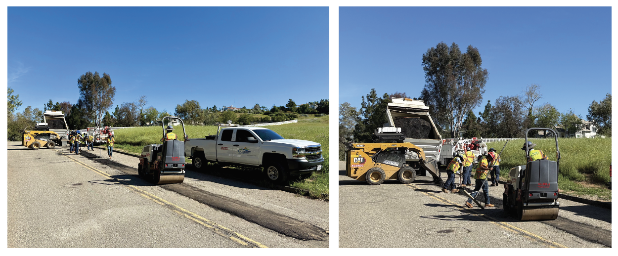 Workers in safety vests use machinery to repair a road, with equipment and a truck nearby under a clear blue sky.