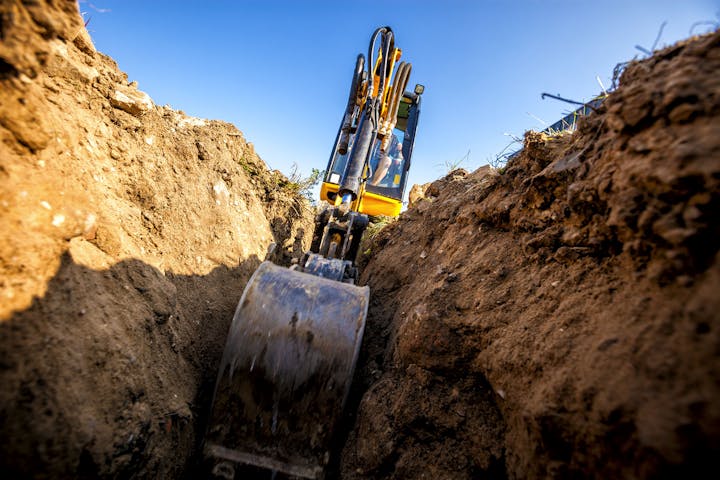 A close-up view of an excavator digging in a trench, showcasing the machinery and surrounding earth under a clear blue sky.