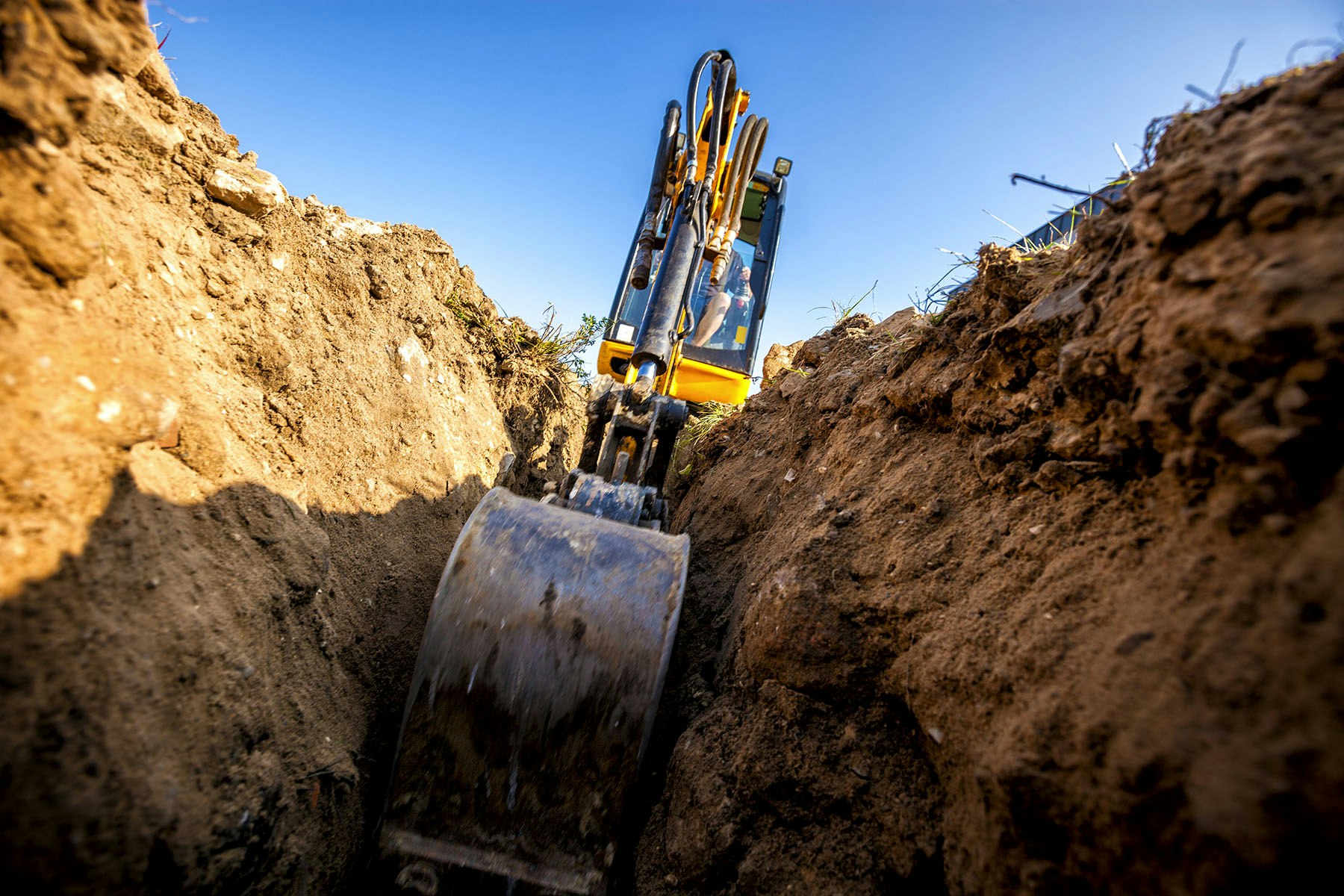 A close-up view of an excavator digging in a trench, showcasing the machinery and surrounding earth under a clear blue sky.