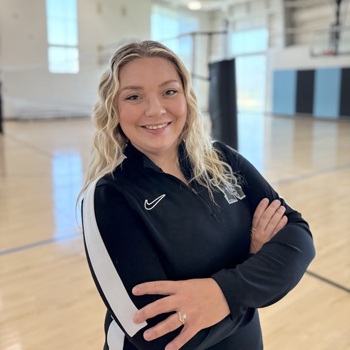 A person smiling with crossed arms in a gym setting.