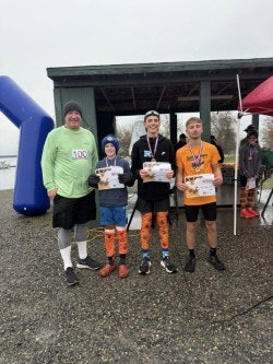 Four people, including a man and three young runners, pose with certificates after a race, wearing colorful attire in a wet environment.