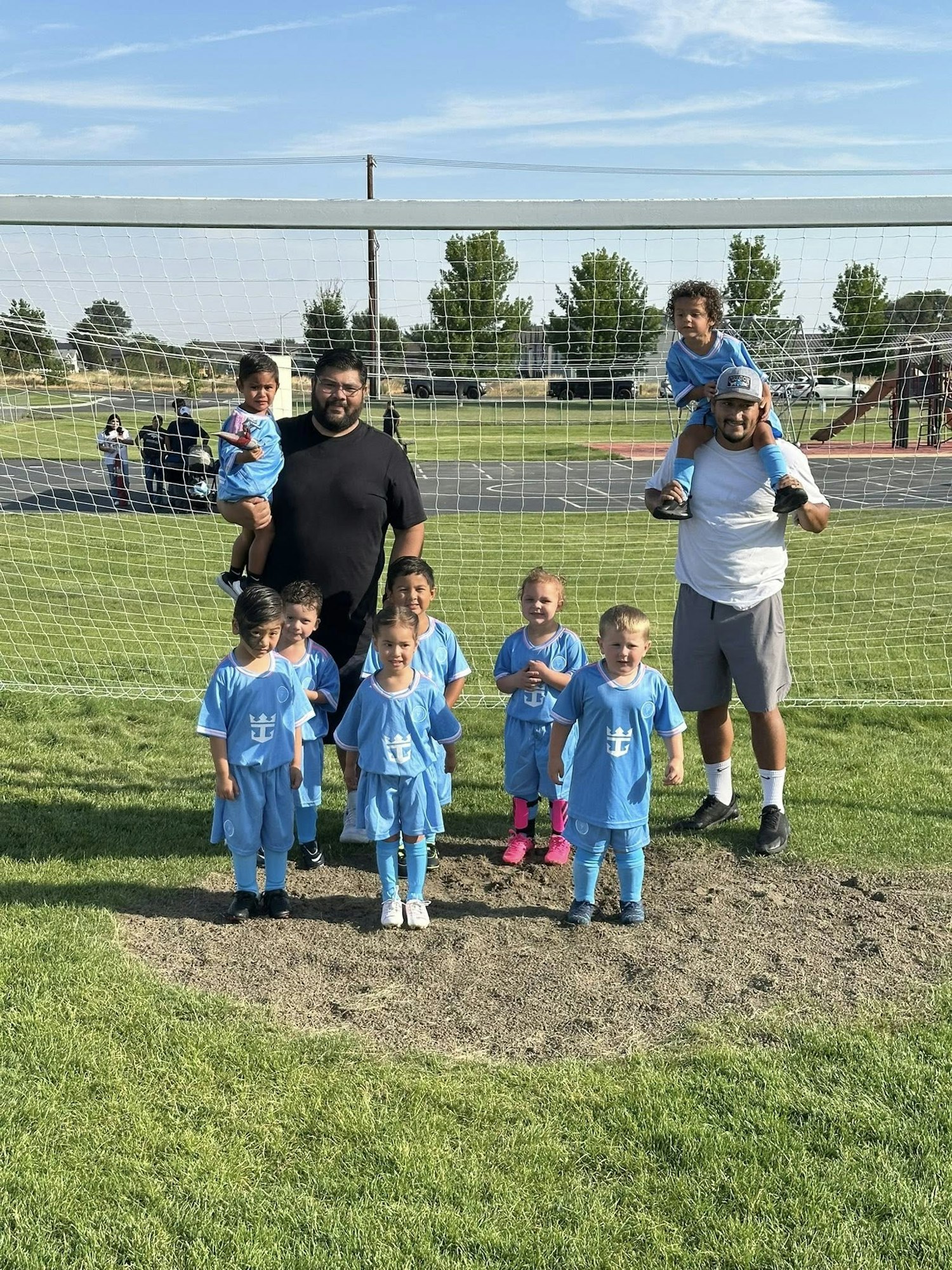 A youth soccer team poses in front of a goal with two adults holding children on their shoulders.