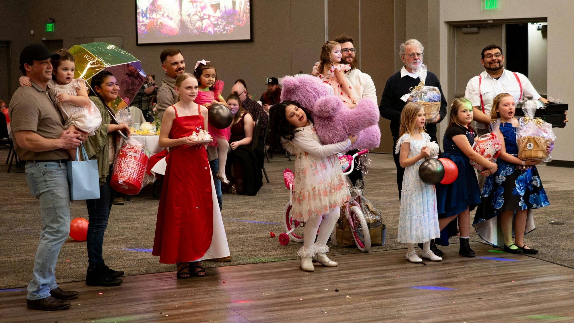 A lively gathering with children and adults, featuring colorful outfits, gifts, and a festive atmosphere in a decorated hall.