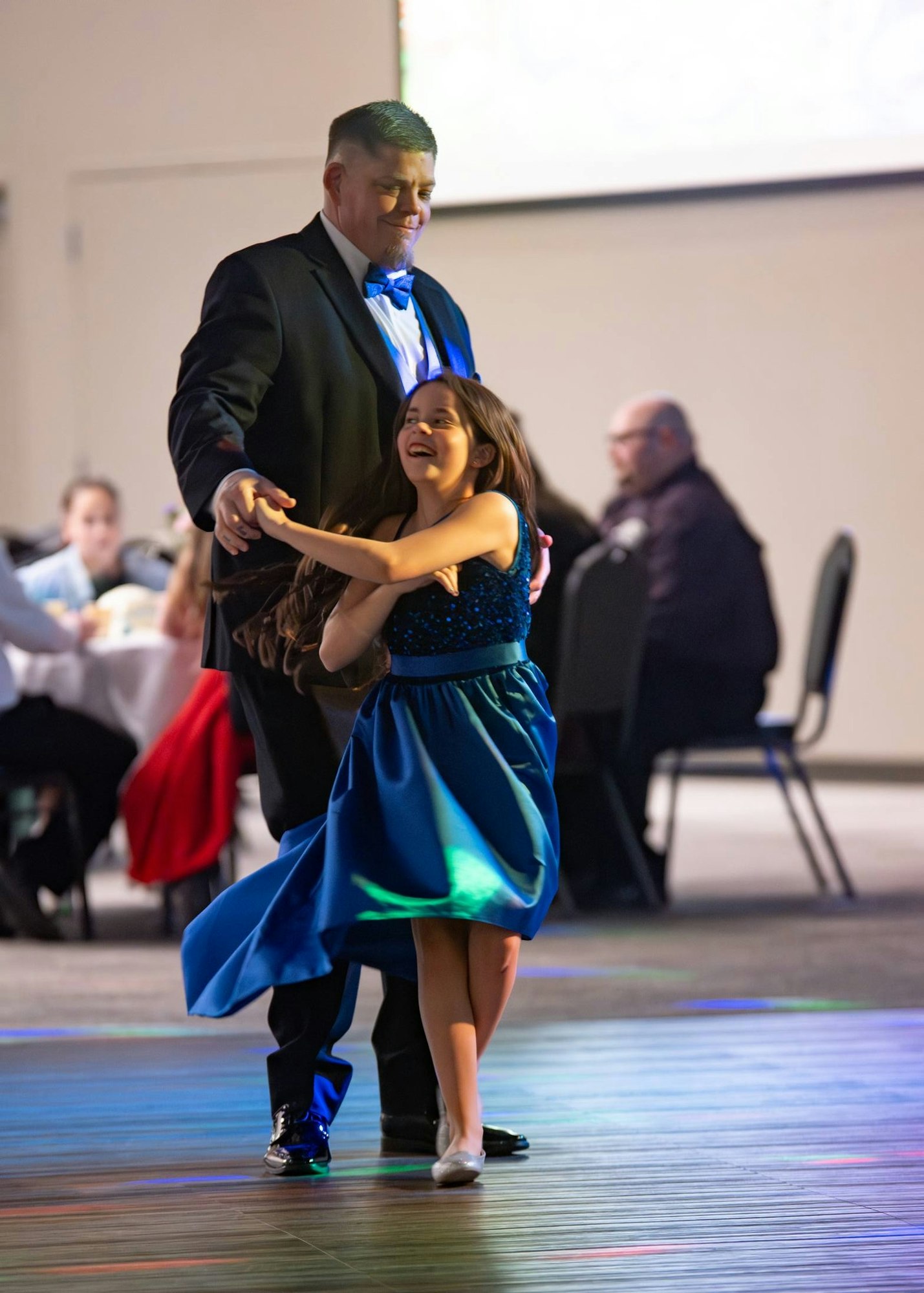 A man and a girl dance joyfully together at a lively event, showcasing a fun and festive atmosphere.