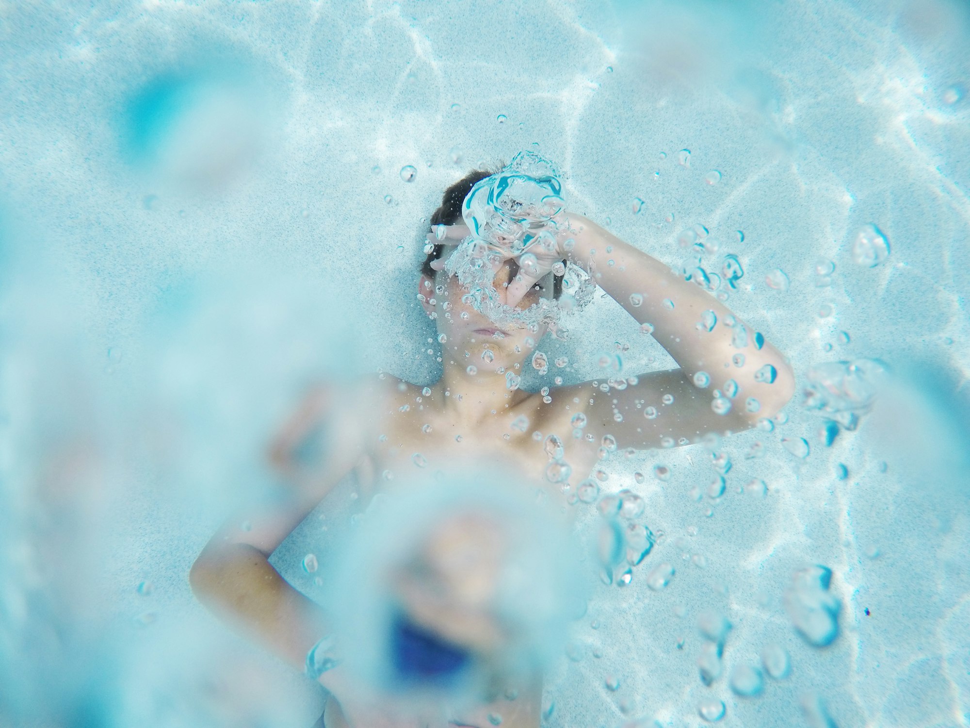 Person underwater with goggles, surrounded by bubbles in a pool.