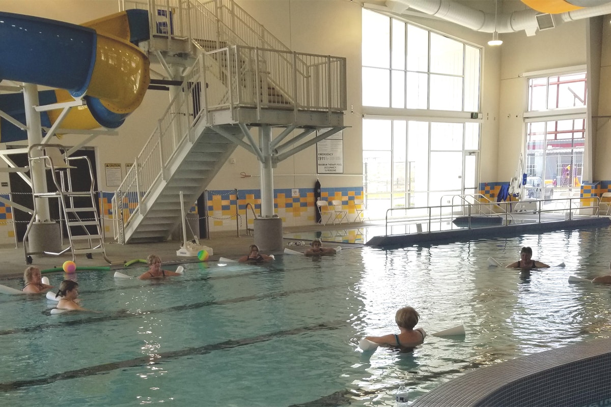 Indoor pool with people, water slide, and stairs.