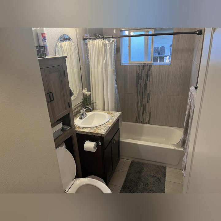 A modern bathroom with a shower-tub combo, sink with granite countertop, mirror, and a wooden cabinet. Neutral colors and decor.