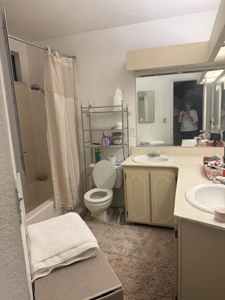 The image shows a bathroom with a bathtub, toilet, sink, and storage, featuring towels and toiletries in a neutral color scheme.