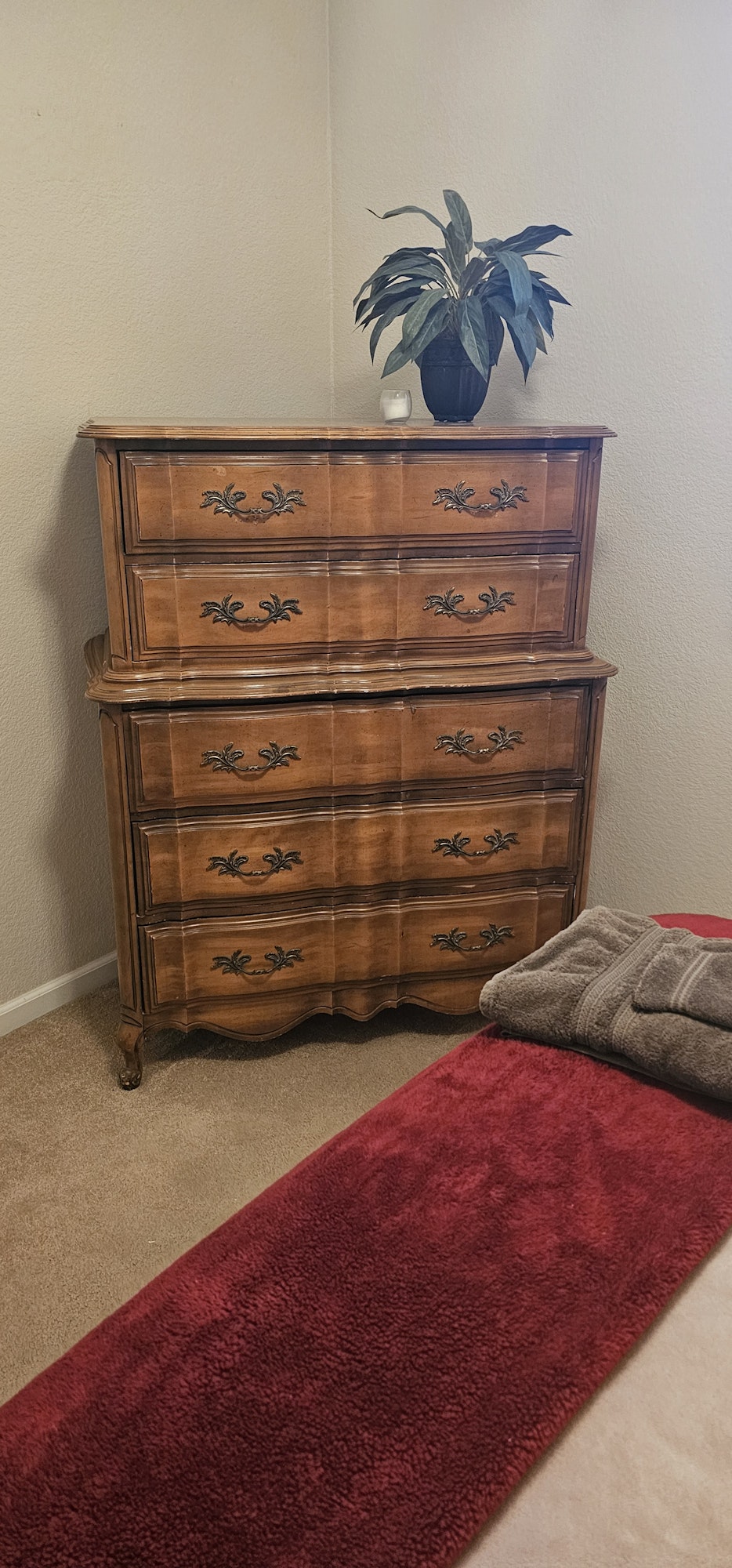 Wooden dresser with decorative details, potted plant on top, red and beige blankets on the side.