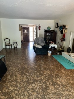 A living room with wood flooring, an armchair, yoga mat, hats on the wall, and a view into a well-lit hallway.