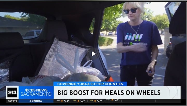 A person with a "Meals on Wheels" shirt stands near a car filled with bags. The news is about "Big Boost for Meals on Wheels" in Sacramento.