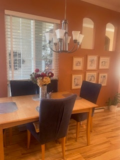 A dining area with a wooden table, purple chairs, a chandelier, and framed artwork on the orange wall.
