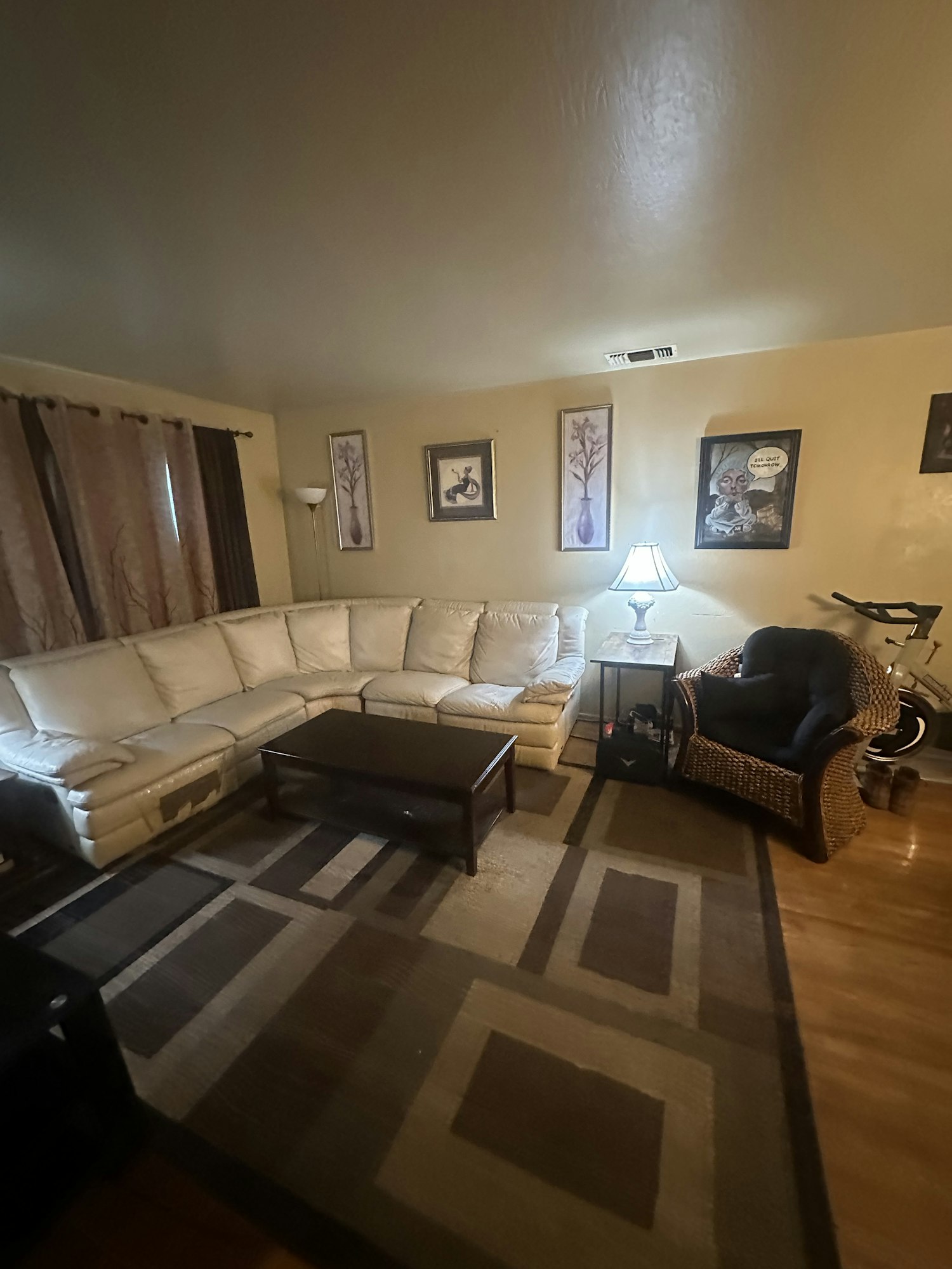 A living room with a beige sectional sofa, geometric rug, wall art, a wicker chair, and a lamp.