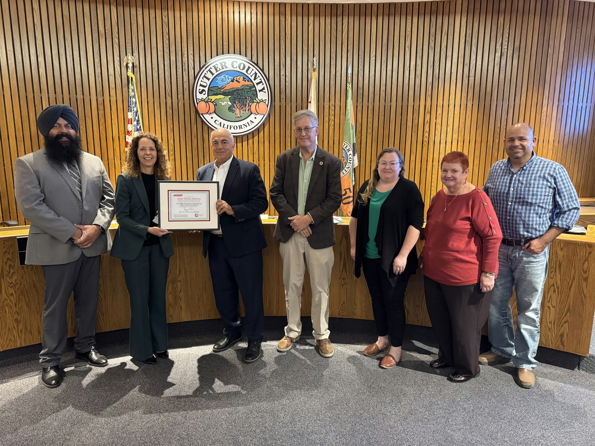 A group of people poses with a certificate at a Sutter County meeting, showcasing community involvement or recognition.