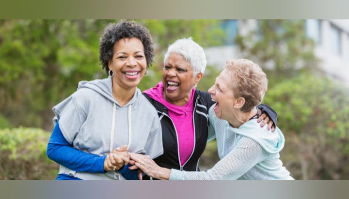 Three smiling women huddled together outdoors, appearing happy and friendly.