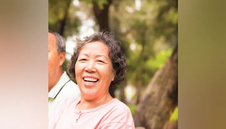A smiling woman outdoors, with trees in the background.
