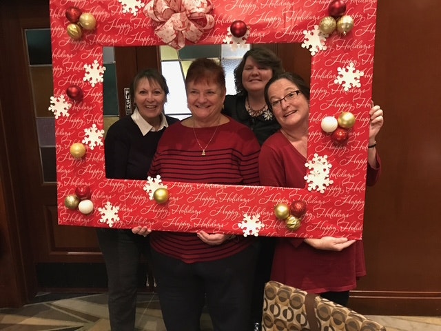 Four women pose together inside a festive photo frame decorated for the holidays.