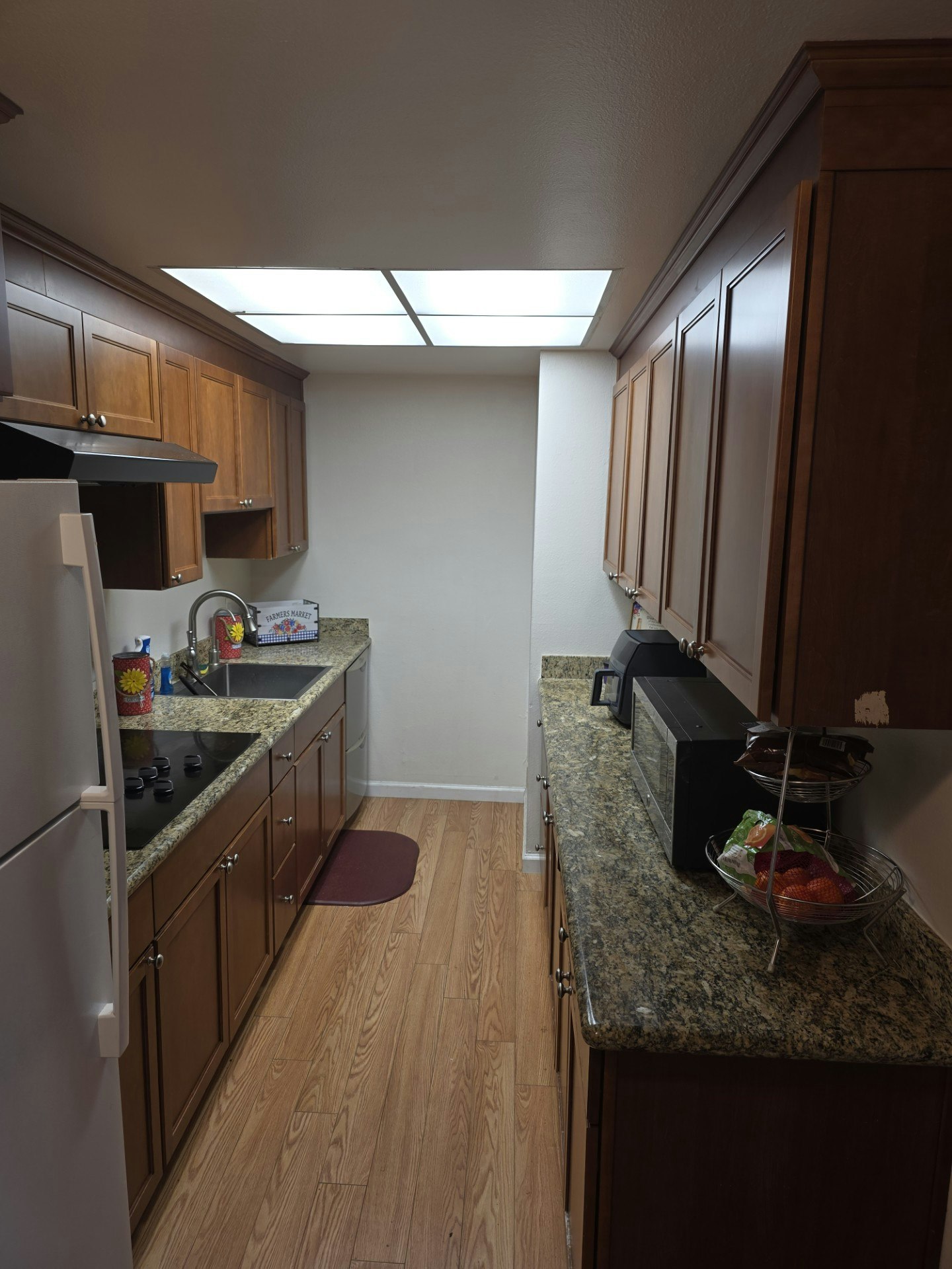A modern kitchen with wooden cabinets, granite countertops, a sink, appliances, and a fruit basket on the counter.