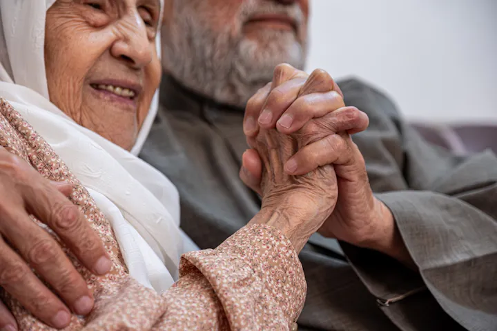 An elderly couple shares a tender moment, holding hands and smiling, showcasing love and connection.