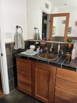Bathroom vanity with sink, mirror, wooden cabinets, towels, and various toiletries on a black countertop.
