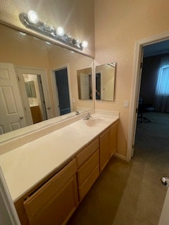A bathroom with a countertop, sink, mirrors, light fixtures, and a door leading to another room.