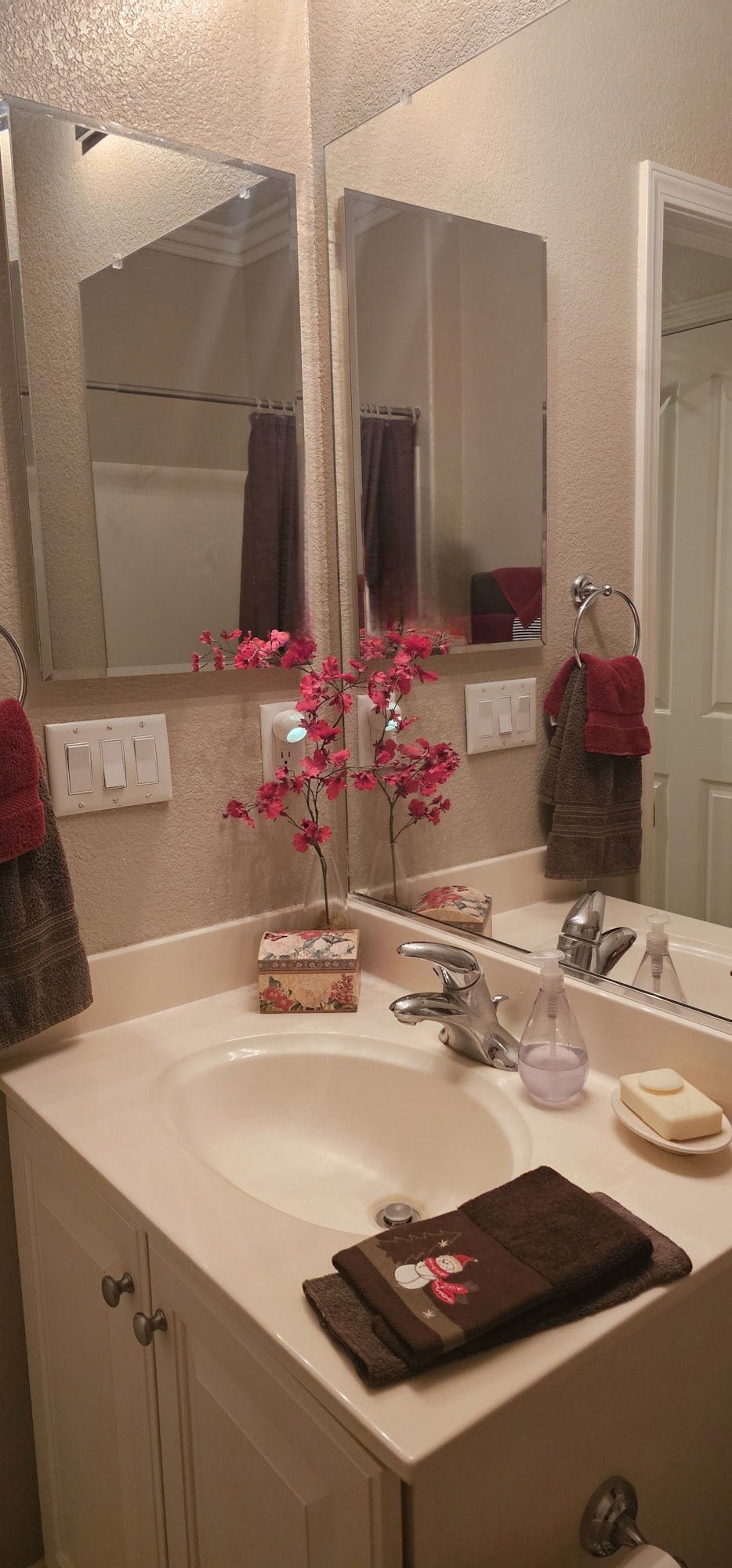 Bathroom sink with red flowers, mirror, soap, towels, and decorative box.