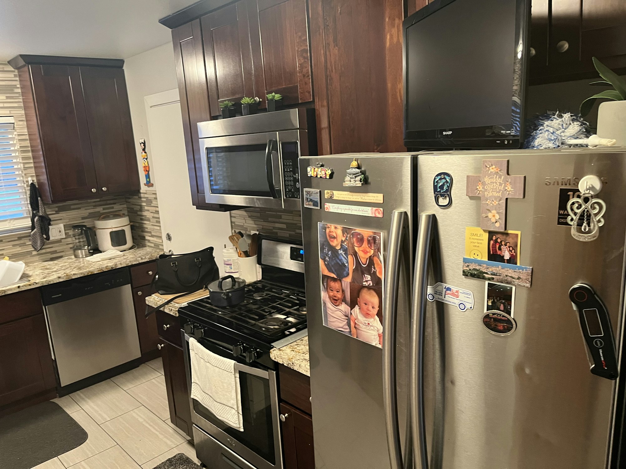 A cozy kitchen with dark wood cabinetry, stainless steel appliances, and a fridge adorned with photos and magnets.