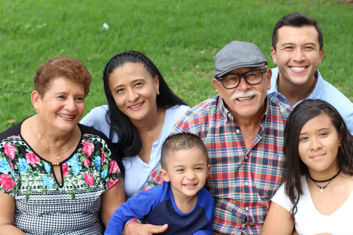 A cheerful family gathering with six members, including children and adults, smiling together outdoors on grass.
