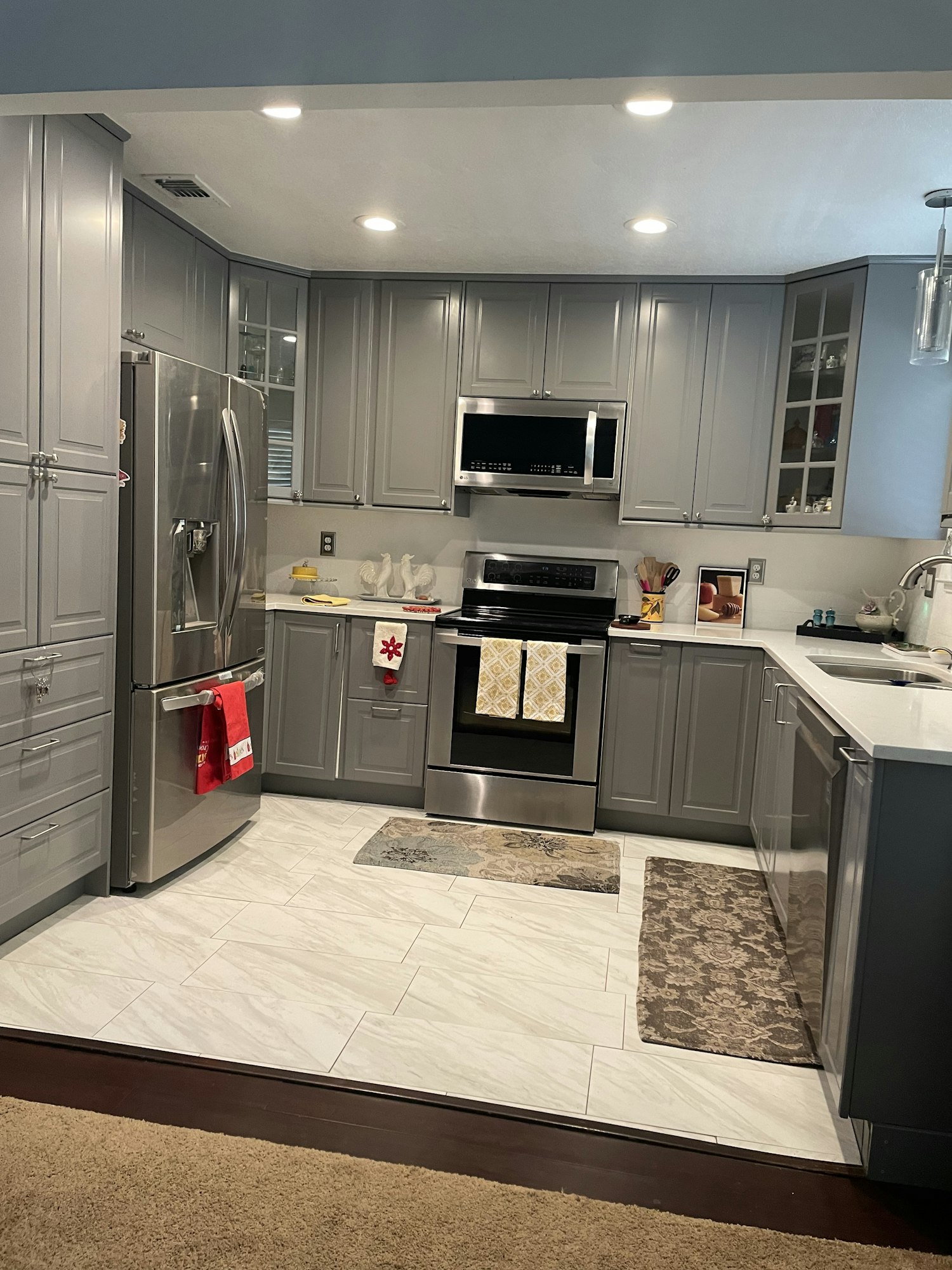 Modern kitchen with gray cabinets, stainless steel appliances, and decorative rugs.