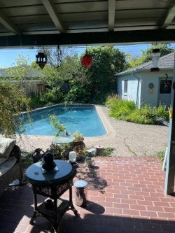 A covered patio with furniture overlooks a swimming pool, surrounded by greenery and a small building in the background.