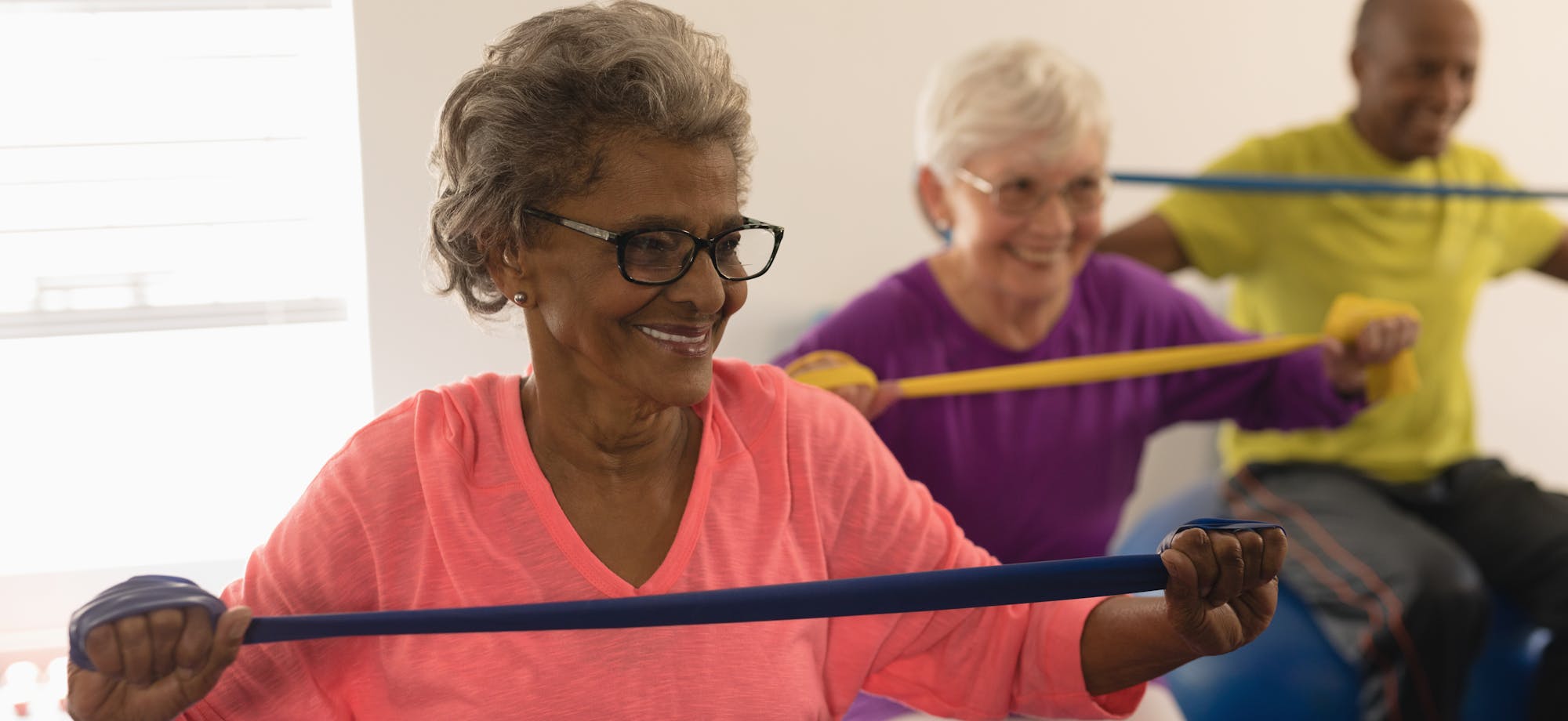 Three seniors exercising with resistance bands, smiling, engaged in a fitness activity.